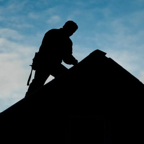 silhouette of a worker on a rooftop set against a blue sky
